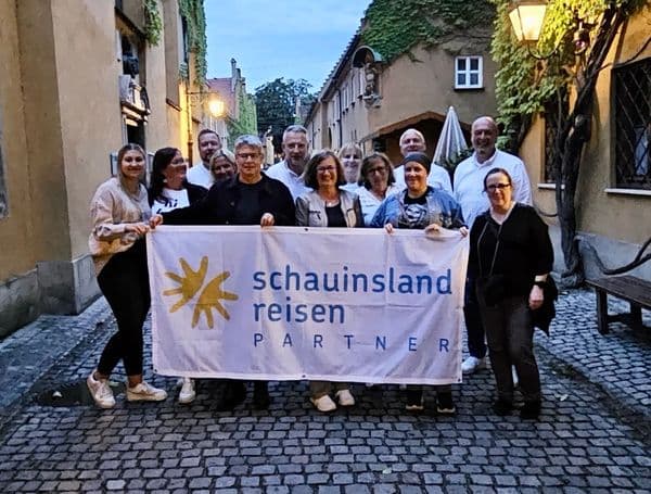 Gruppe von Kooperationspartnern mit dem damaligen Geschäftsführer bei einem Regio-Treff in Chemnitz: Die Teilnehmenden stehen in einer schmalen, historischen Gasse bei Abendlicht und halten gemeinsam ein Banner mit der Aufschrift „schauinsland reisen PARTNER“.