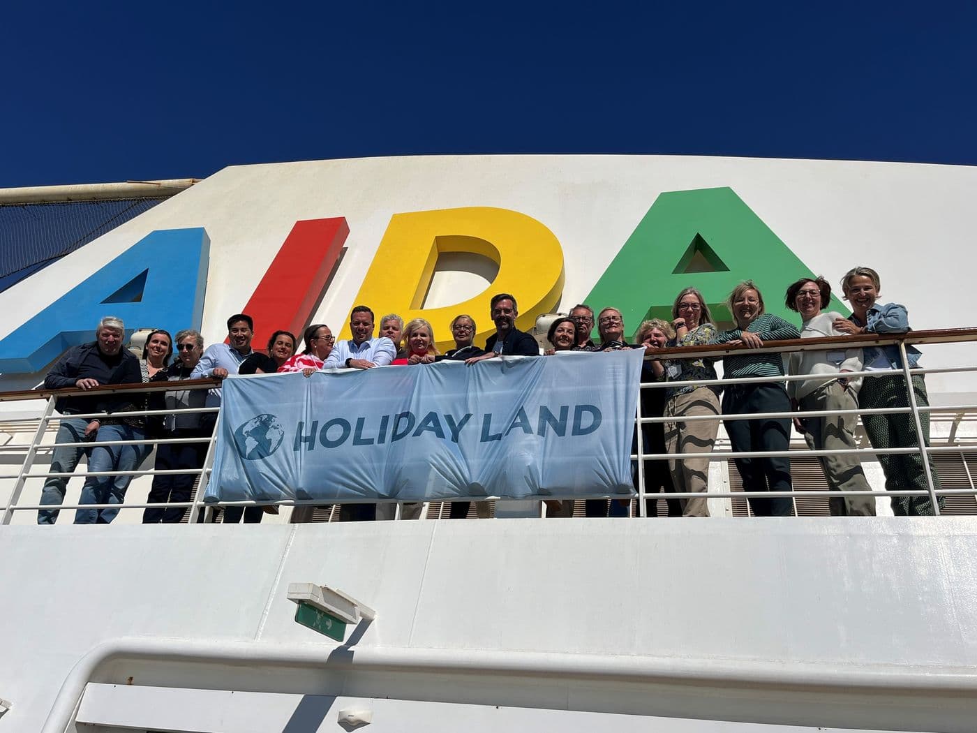 Die Teilnehmer der MOVE-Inhaberreise an Bord der AIDAsol vor dem Logo am Schornstein halten ein Banner mit der Aufschrift HOLIDAY LAND